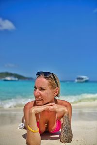 Smiling woman lying on shore at beach against sky