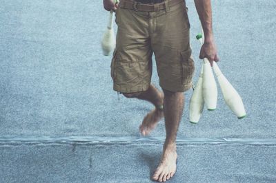 Low section of man holding juggling pins and walking on floor