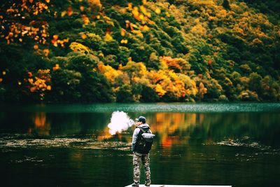 Man exhaling smoke while standing on pier by lake during autumn