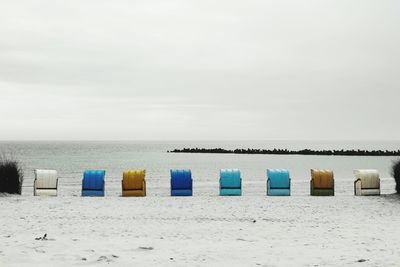 Hooded chairs on beach against sky