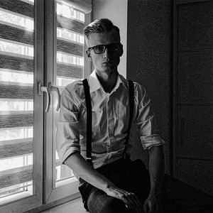 Portrait of young man wearing eyeglasses sitting on window sill