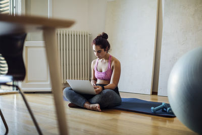 Young sportive woman using laptop on yoga mat