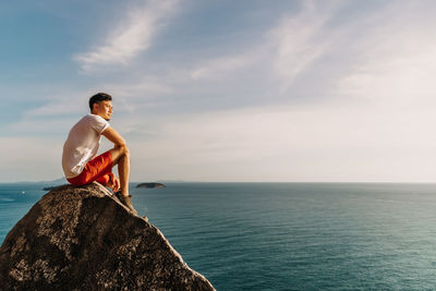 Man standing on rock by sea against sky