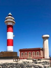 Low angle view of lighthouse against building against clear blue sky