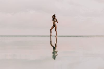 Full length of seductive young woman standing by infinity pool against sea and sky
