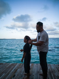 Side view of father tying daughter hair while standing on pier