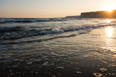 Waves approaching beach sand during golden sunset