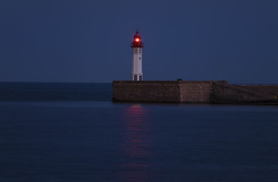 Lighthouse with red light by sea against sky at night. almeria, spain.