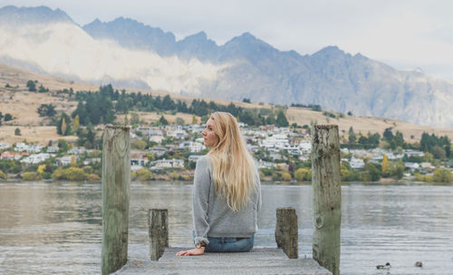 Rear view of young woman sitting on pier over lake