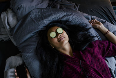 High angle view of woman lying on bed with cucumber slices on eyes