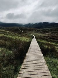 Boardwalk on field against sky