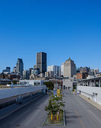 Road by buildings against clear blue sky