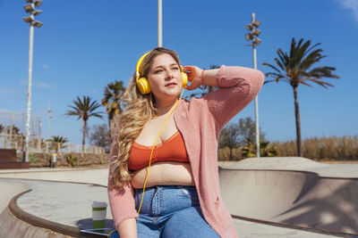 Young woman listening music sitting against sky