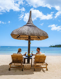 Rear view of woman sitting on beach against sky