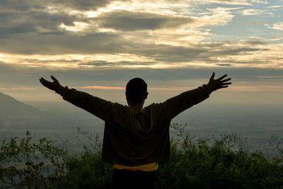 Rear view of man standing by plants against sky during sunset