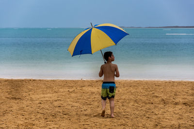 Rear view of boy walking on beach with umbrella