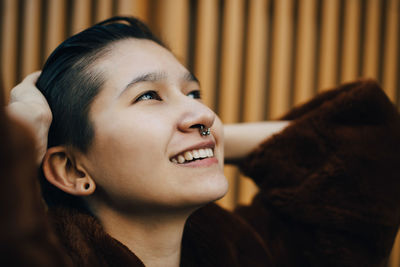 Smiling woman with hands in hair standing against wooden wall