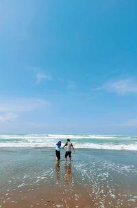 Rear view of men on beach against sky