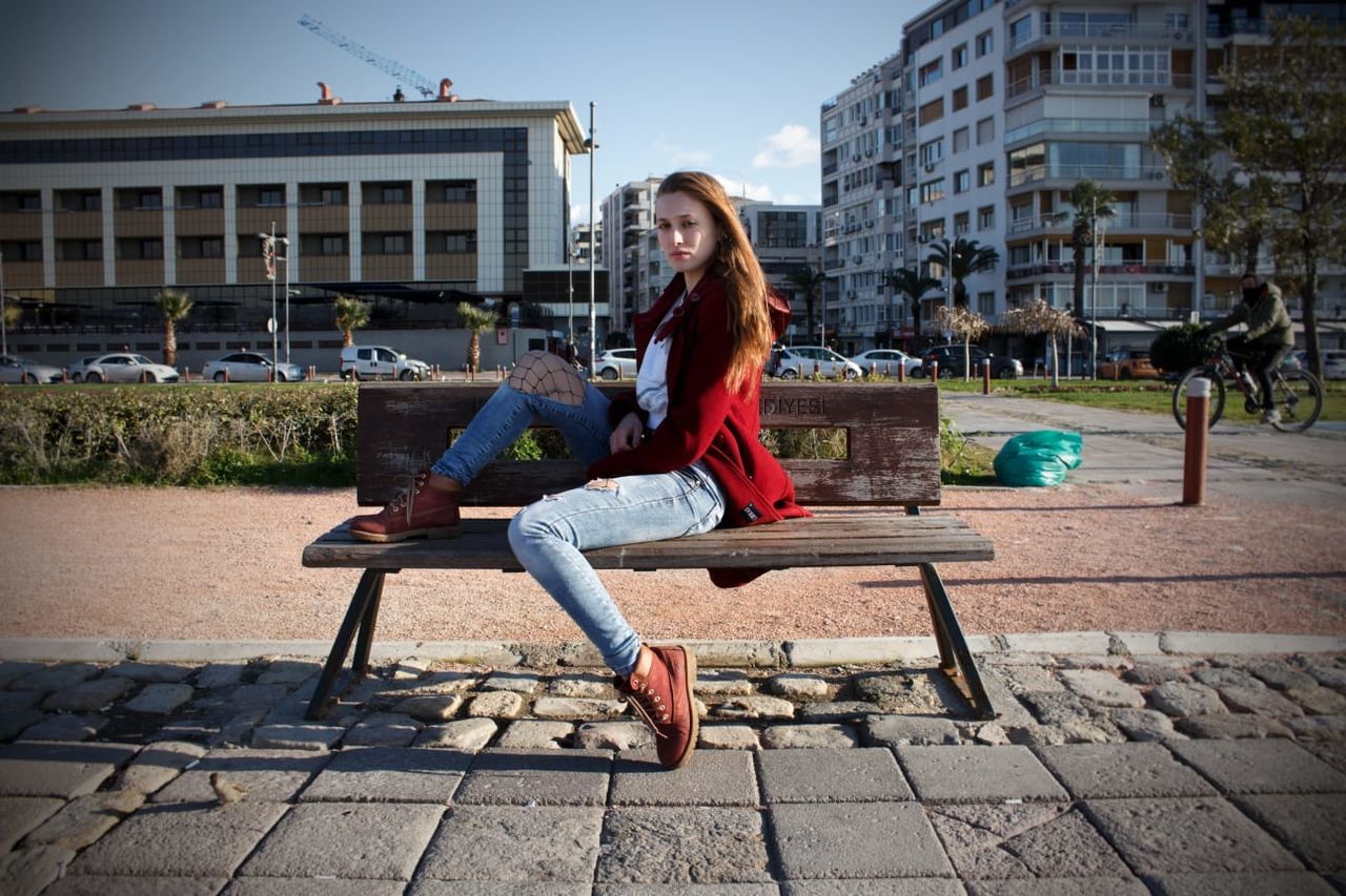 full length, sitting, young adult, one person, casual clothing, young women, architecture, bench, building exterior, adult, leisure activity, hairstyle, long hair, built structure, lifestyles, hair, day, real people, portrait, outdoors, beautiful woman, paving stone, teenager