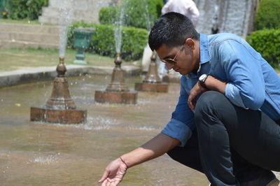Young man wearing sunglasses crouching by fountain