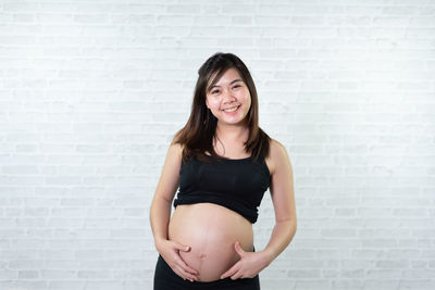 Portrait of smiling pregnant woman standing against wall