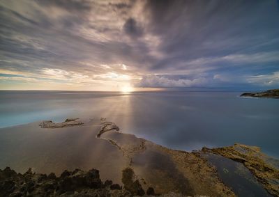 Scenic view of sea against cloudy sky during sunset