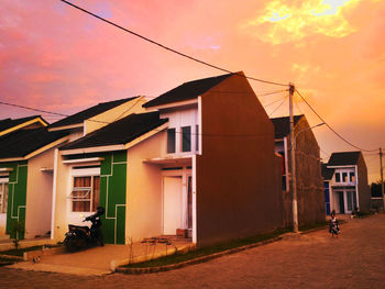 Exterior of houses by building against sky during sunset