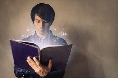 Young woman reading book against wall