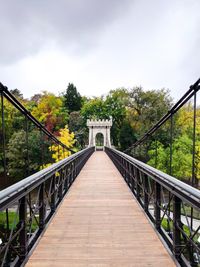 Footbridge along plants and bridge against sky