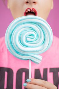 Close-up of woman holding blue lollipop standing against pink background