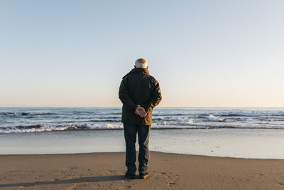 Rear view of man standing at beach against clear sky