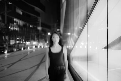 Portrait of young woman standing against illuminated city at night