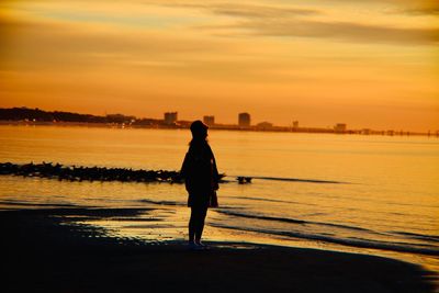 Side view of silhouette mature woman standing at beach against sky during sunset