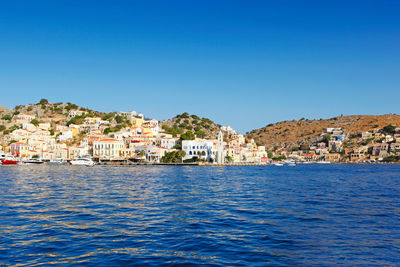 View of townscape by sea against clear blue sky