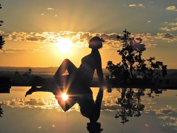 Side view of silhouette woman sitting by water during sunset