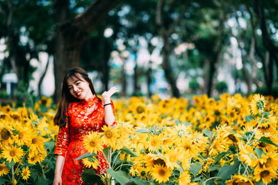 Young woman standing by yellow sunflowers on field