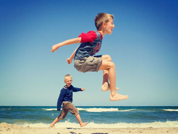 Full length of a boy jumping on beach against clear sky