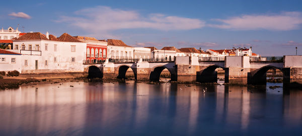 Arch bridge over river by buildings against sky in city