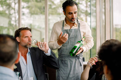 Businessman with wine bottle explaining colleagues at convention center