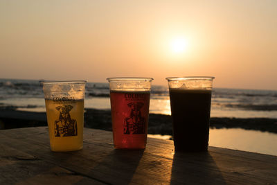 Close-up of beer on table at beach against sky during sunset