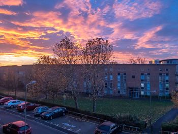 Cars on road by buildings against sky during sunset