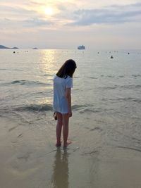 Rear view of young woman standing on seashore during sunset