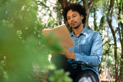 Low angle view of young man sitting against trees