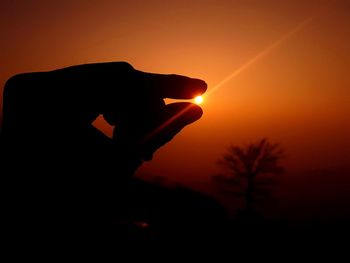 Optical illusion of silhouette hand holding sun in sky at sunset