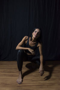 Portrait of a woman sitting on the floor against black background. 