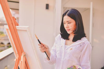 Thoughtful woman painting on canvas