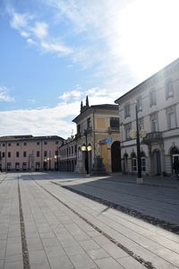 Empty road by buildings in city against sky