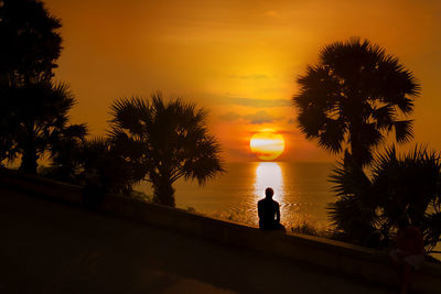 Silhouette man standing by palm trees against sky during sunset