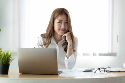 Portrait of young woman using phone while sitting on table
