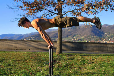 Full length of shirtless man on tree against sky